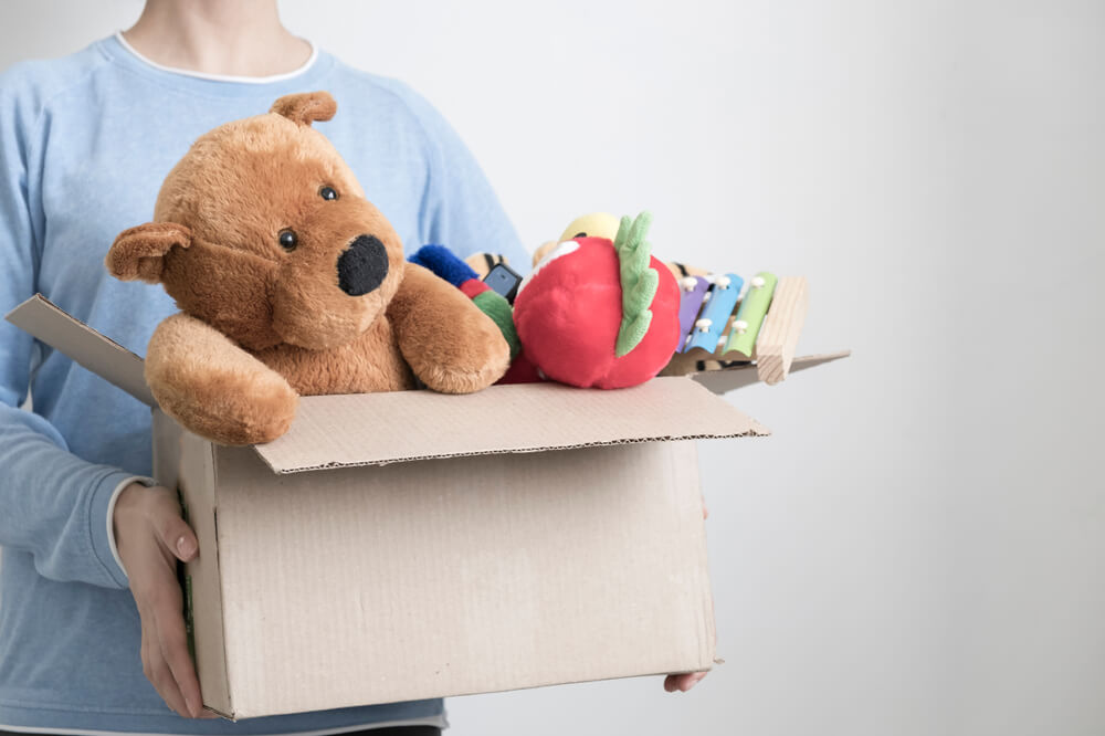 Someone wearing a light blue long sleeved shirt with a white one underneath. They are holding a cardboard box filled with toys for children