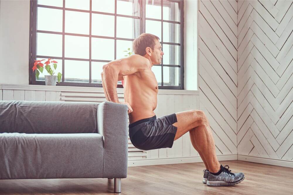 home workouts shirtless muscular male does exercise leaning on a sofa at home