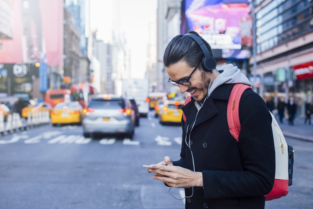 man walking in a NYC crowded street while looking at his smartphone with his headphones on