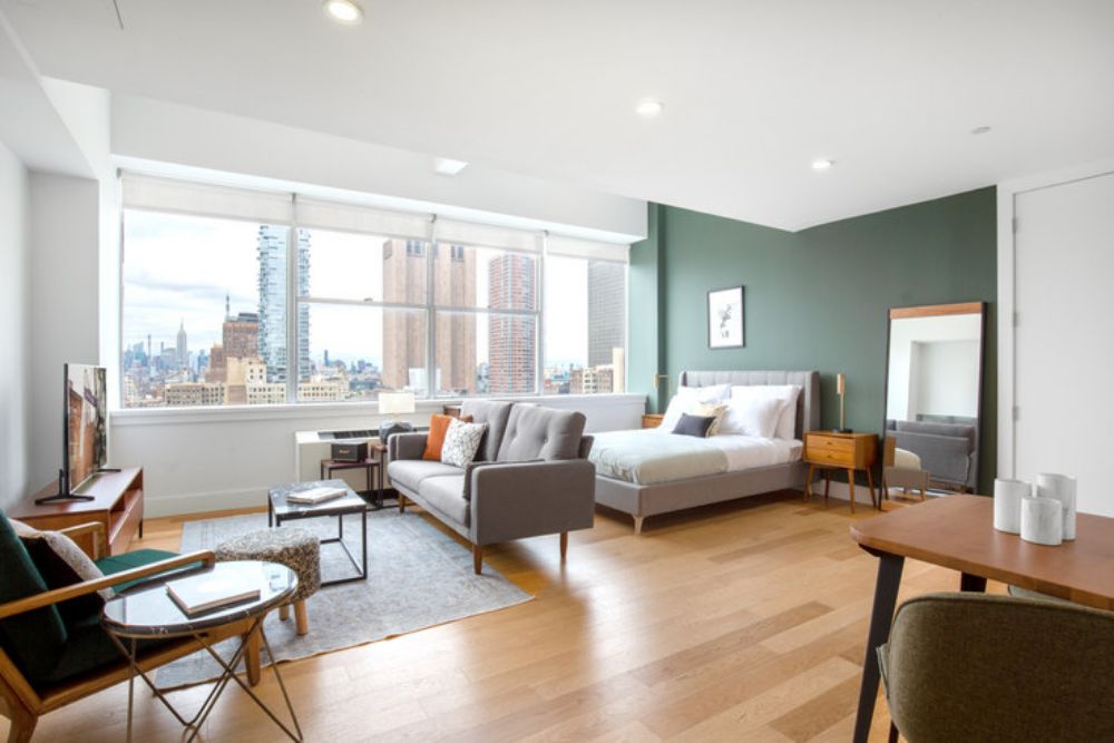 a blueground studio apartment in nyc with a dark green accent wall and a view outside of the city 