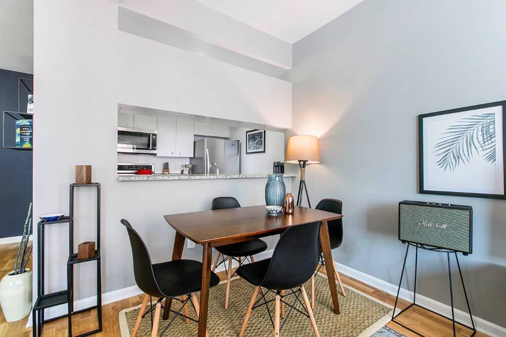 A wooden dining table with four black chairs around it sits in the corner of an apartment in New York City that is furnished and managed by Blueground
