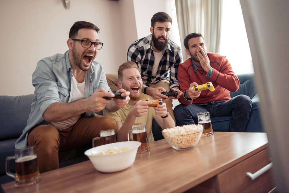 Four men are sitting on the couch playing video games and drinking beers in Seattle