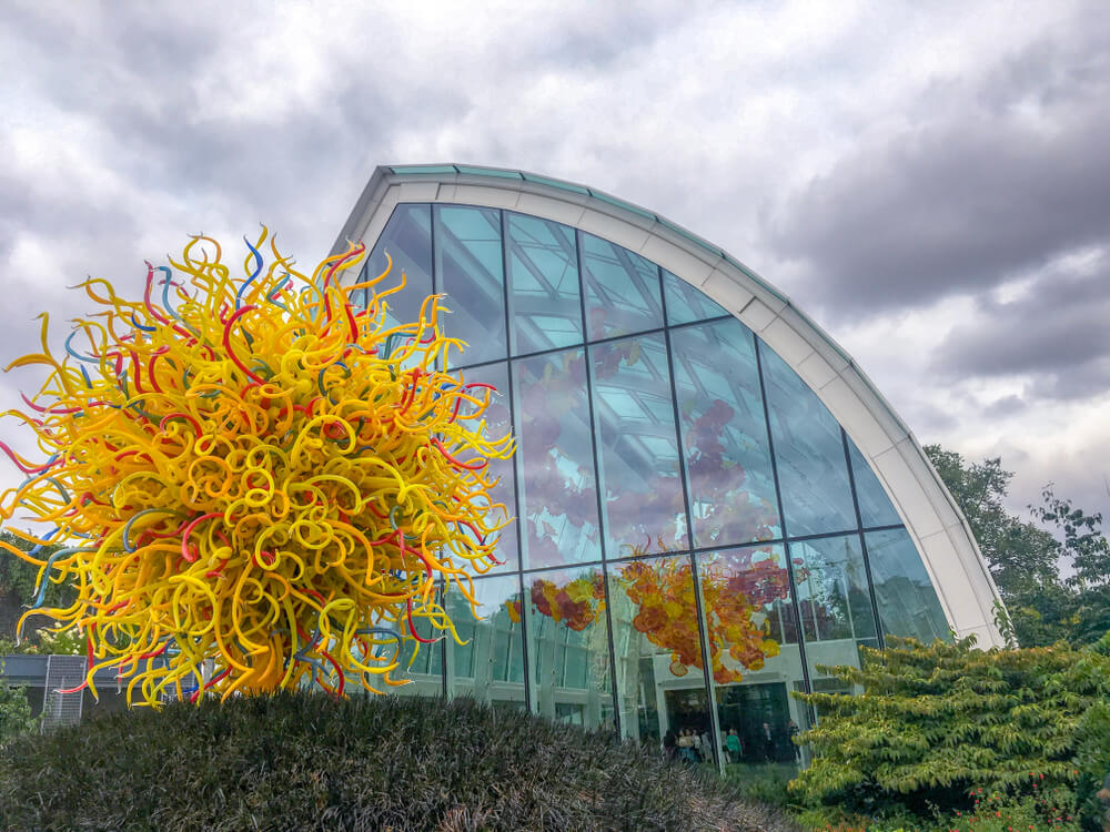 A large dome shaped glass building with a modern art yellow and red sculpture in front