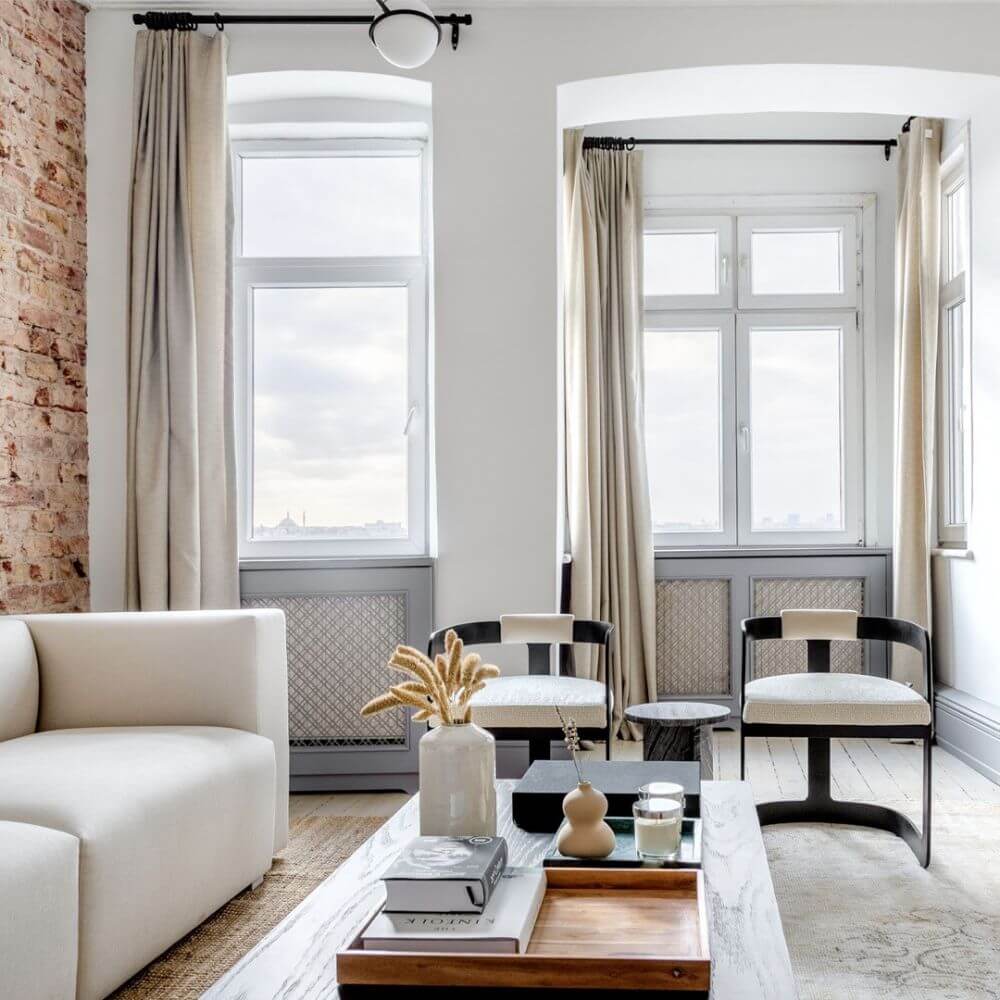 A furnished bespoke apartment managed and designed by Blueground with a white couch and a brick accent wall. There are two black and white chairs in front of a wooden coffee table with lots of decorative elements on top.
