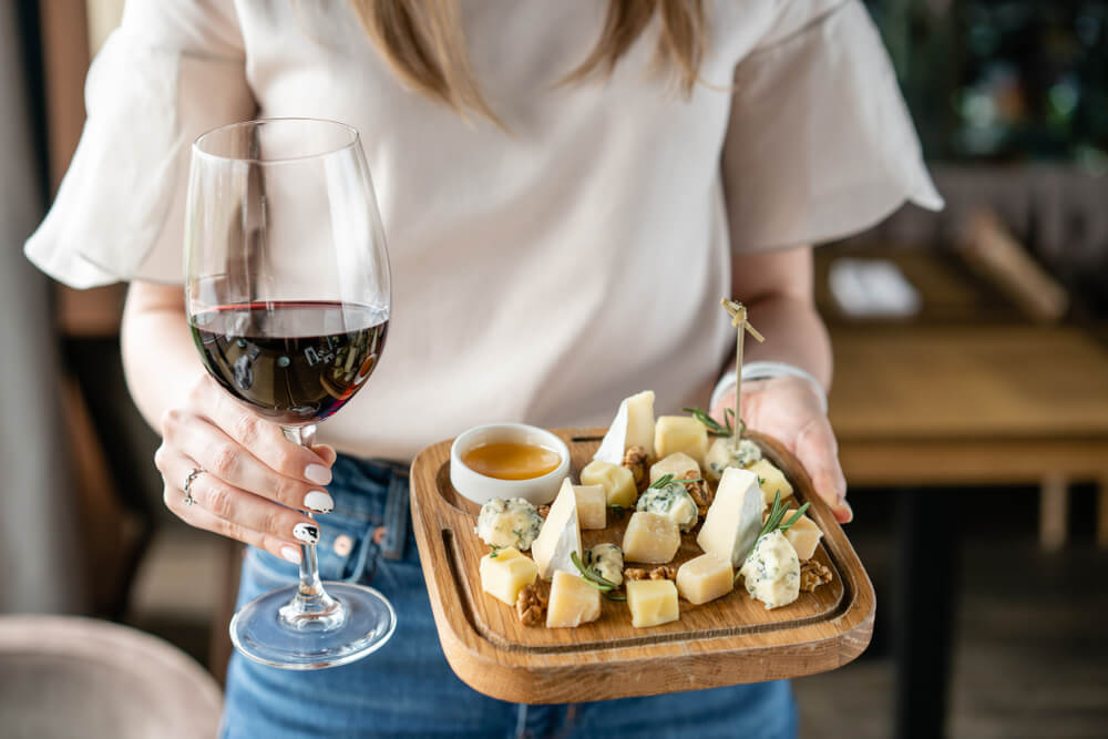 girl holding a cheese plate and a glass of red wine