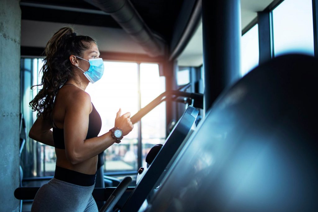a woman running on a treadmill with a surgical mask on