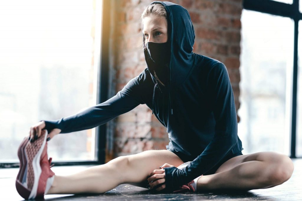 a girl, wearing a face mask stretching her leg on the floor