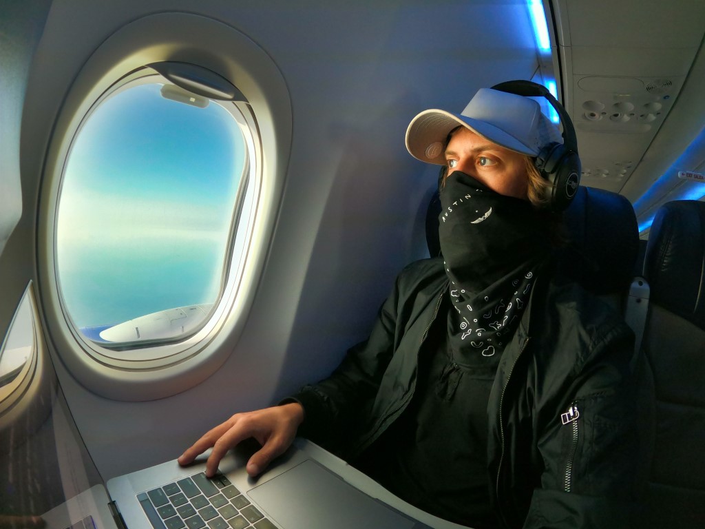 A man wearing a mask in an airplane working on his laptop