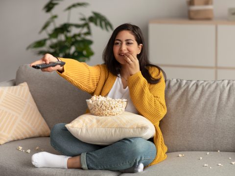 Woman watching tv while eating popcorn